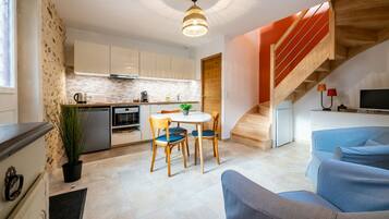 A modern kitchen with white cabinets, a dining area with a table and chairs, and a staircase leading to a living room with a blue sofa.