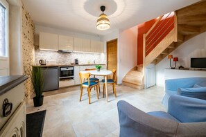 Une cuisine moderne avec des meubles blancs, un coin repas comprenant une table et des chaises, et un escalier menant à un salon doté d’un canapé bleu.