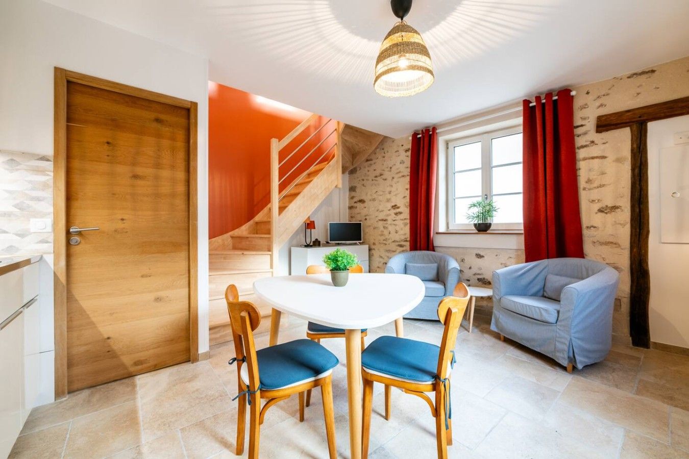A modern living room with a white table, blue chairs, a sofa, and a staircase.