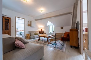 A spacious living room with a high ceiling, a wooden cabinet, a sofa, a coffee table, and a television. - House, Lot | Hot Tub • Fire pit • Art & Deco (Bourdenay)