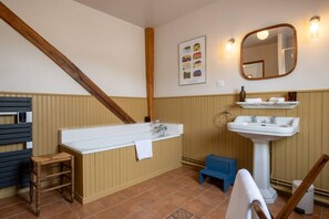 Ein Badezimmer mit einer Badewanne, einem Waschbecken, einem Spiegel und einem hölzernen Hocker.