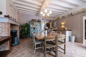 Una cocina amplia con comedor, que cuenta con una chimenea de ladrillo, una mesa de madera grande y una lámpara colgante.