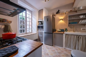 A kitchen with a gas stove, a red pot, a refrigerator, and a window with curtains. - House, Lot | Hot Tub • Fire pit • Art & Deco (Bourdenay)