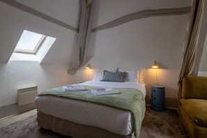 Ein Schlafzimmer mit Dachfenster, einem Bett mit Kissen, einer Nachttischlampe, einem blauen Nachttisch und einem gelben Sessel.