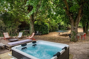 Un jacuzzi rodeado de sillones de descanso y una mesa de ping pong en un área boscosa al aire libre.
