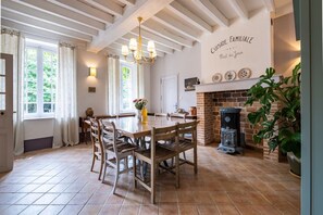 A dining area with a wooden table and chairs, a chandelier, a brick fireplace, and a wall with a sign. - House, Lot | Hot Tub • Fire pit • Art & Deco (Bourdenay)