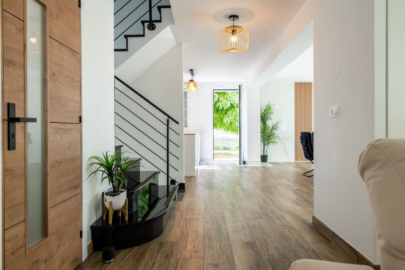 A modern interior with a staircase, wooden flooring, a potted plant, and a hanging light fixture.