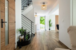 Et moderne interiør med trappe, trægulv, en potteplante og en hængende lampe.