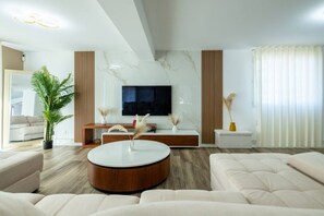 A modern living room with a round coffee table, sofas, a flat-screen TV, and decorative plants. - Le Panoramique | Exceptional Home • 12 trips (Crécy-la-Chapelle)