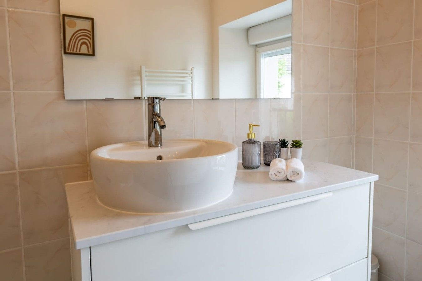 A bathroom with a white sink, a mirror above it, and a window.