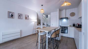 A modern kitchen with a dining area, white walls, and wooden flooring.