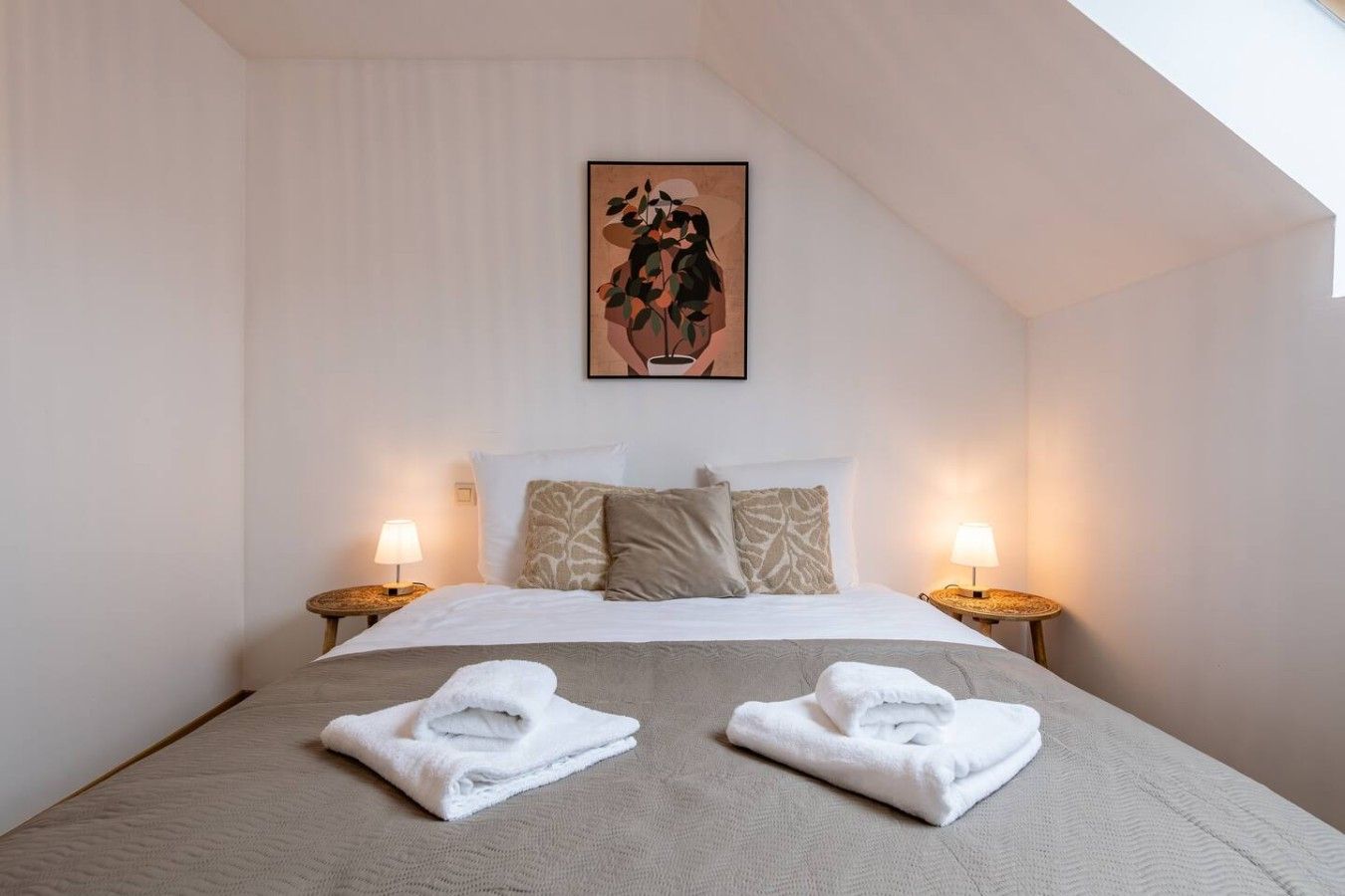 Een hotelkamer met een bed, twee bedlampen, een schilderij en twee handdoeken op het bed.
