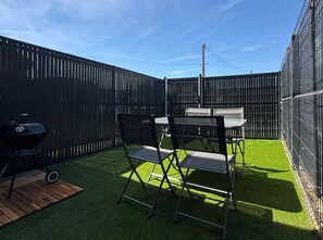 A fenced backyard with artificial grass, a grill, and foldable chairs.