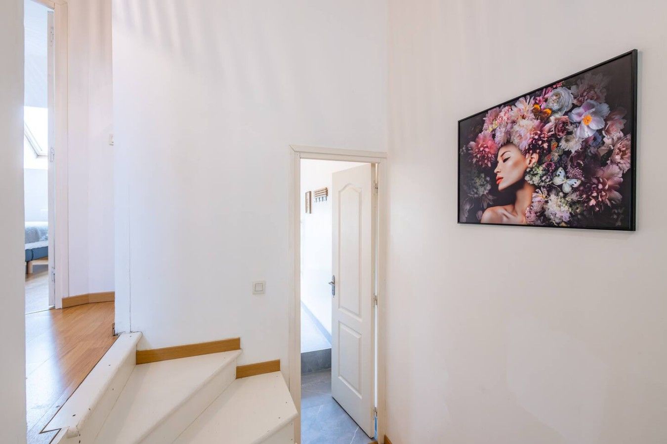 Ein Flur mit einer Treppe, die zu einem anderen Raum führt, einer Tür am Ende und einem gerahmten Blumenbild an der Wand.