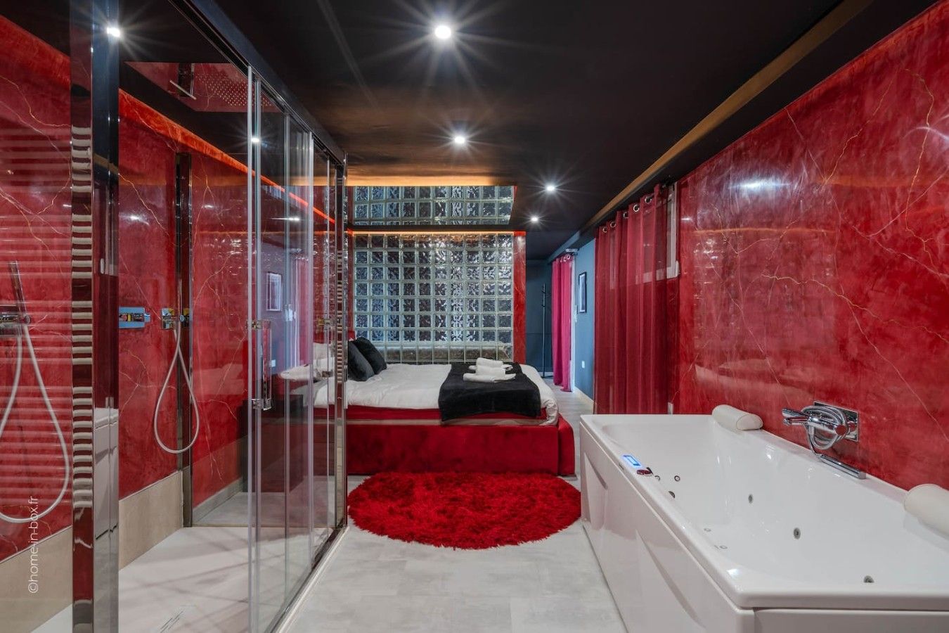 Une salle de bain moderne avec une douche à parois de verre, une grande baignoire et un lit agrémenté d’un tapis rouge.