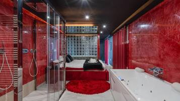 Une salle de bain moderne avec une douche à parois de verre, une grande baignoire et un lit agrémenté d’un tapis rouge.