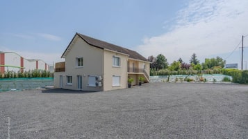 Un bâtiment à deux étages, doté d’un toit plat, d’un balcon et d’une allée gravillonnée.