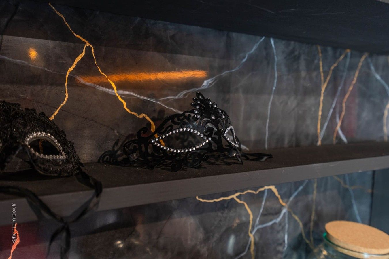 A display of black masks with rhinestones on a shelf against a wall with a marble-like texture and lightning effects.