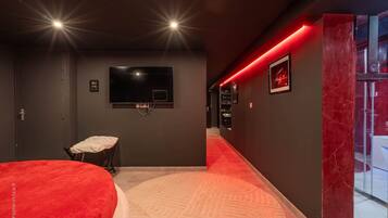 Une chambre moderne dotée d’un téléviseur à écran plat, d’une table de massage et d’un mur d’accent rouge.