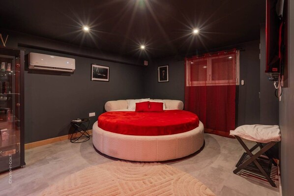 Una cama redonda con cubrecolcha rojo, una mesita de noche pequeña y una cortina roja.