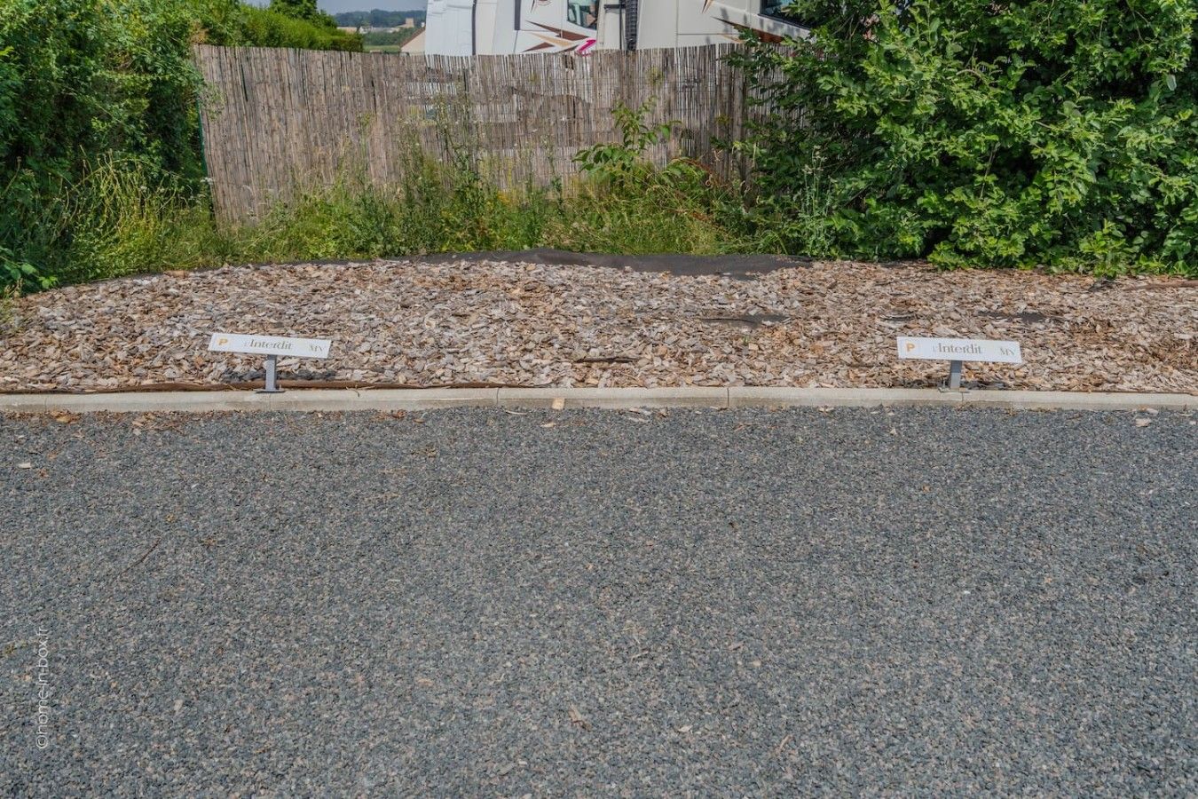 Une zone recouverte de gravier avec deux panneaux indiquant les places de stationnement.