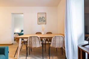 A dining area with a wooden table, wicker chairs, a vase with dried plants, and a framed artwork on the wall. - A Little Getaway—Air-conditioned home, barbecue, renovated (Longueville)