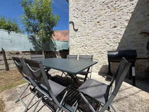 An outdoor patio with a table and chairs, a barbecue grill, and a stone wall. - A Little Getaway—Air-conditioned home, barbecue, renovated (Longueville)