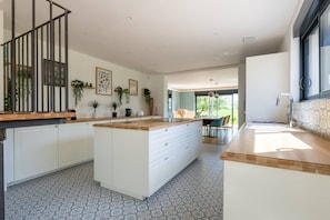 A modern kitchen with a central island, white cabinetry, and a dining area with a view. - L'Évasion – House with pool and hot tub, sleeps 14 (Lescherolles)
