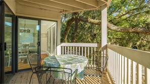 Ein Balkon im Freien mit Tisch und Stühlen, umgeben von Bäumen und einer Holzterrasse.