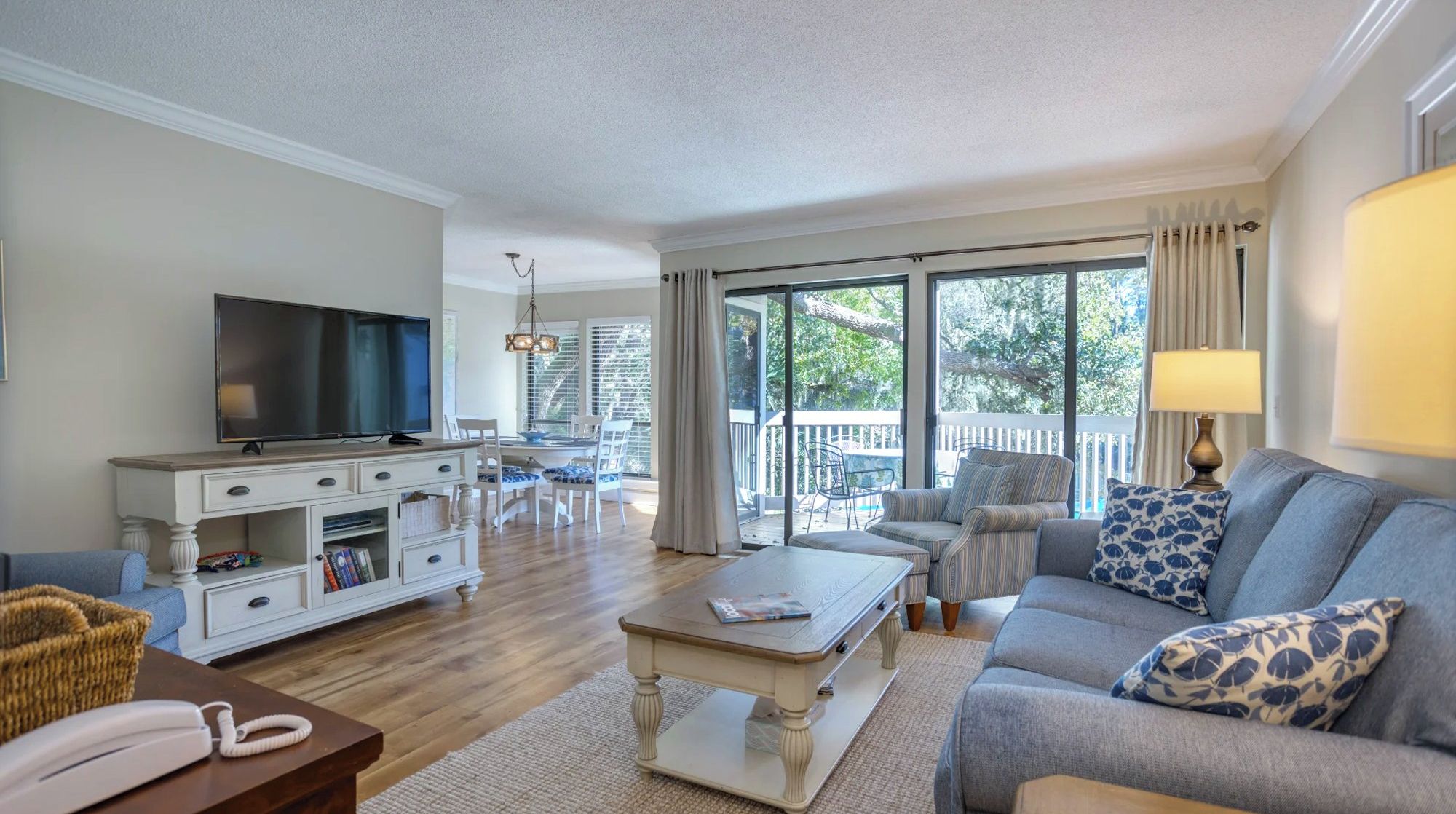 Placid blue tones and creamy wood finishes ground this airy living room, where floor to ceiling glass invites the afternoon glow inside. A plush sofa and woven textures create a serene space for slow mornings spent watching the oaks sway outside.