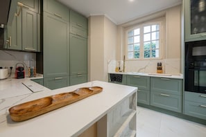 A kitchen with green cabinets, a marble countertop, and a window with a view of greenery. - Villa Les Roches - Comfort - Relaxation - Pool (La Ferté-Gaucher)