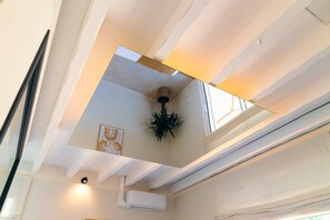 Una habitación con aire acondicionado instalado en el techo, una planta en maceta y una obra de arte enmarcada.
