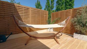 Un hamac est suspendu entre deux poteaux en bois, dans un espace patio, avec une clôture en bois en arrière-plan.