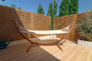 Eine Hängematze, die zwischen zwei Holzpfählen in einem Patio-Bereich gespannt ist, mit einem Holenzaun im Hintergrund.
