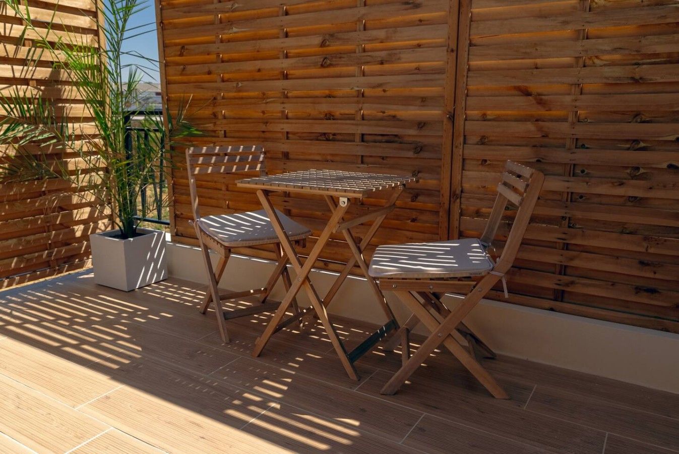Une terrasse extérieure avec une table et des chaises en bois, une plante en pot et un mur en bambou.