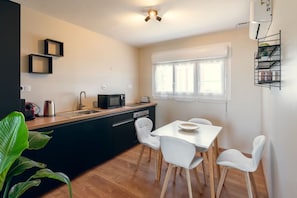 A compact kitchen with a microwave, kettle, and toaster, a dining table with chairs, and a window with curtains. - The elegant, air-conditioned, and renovated (La Ferté-Gaucher)