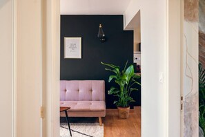 Une pièce avec un canapé rose, un mur noir, une citation inspirante encadrée, une plante en pot et une petite table.