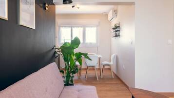 A modern living room with a sofa, a dining table with chairs, and a large plant.