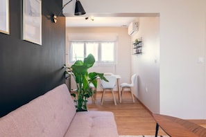 A modern living room with a sofa, a dining table with chairs, and a large plant.