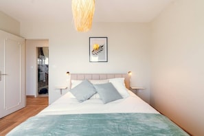 A bedroom with a bed, bedside lamps, a framed artwork, and a door leading to another room.