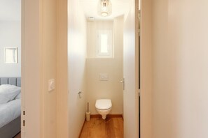Passadís estret que condueix a un bany amb un vàter, un assecador de mans i un interruptor de llum a la paret.