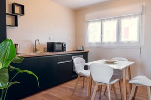 Une cuisine compacte équipée d’un four à micro-ondes, d’un grille-pain et d’un évier. On y trouve une table à manger avec des chaises, ainsi qu’une fenêtre avec des rideaux.