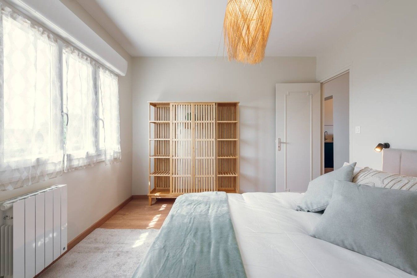 A bedroom with a bed, a wardrobe, and a window with sheer curtains.