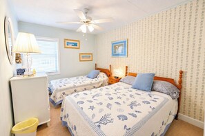 Ein Schlafzimmer mit zwei Betten, einem Deckenventilator, einer Lampe und einem kleinen Mülleimer.