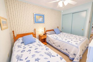 Quarto com duas camas, mesa de cabeceira, quadro emoldurado e uma porta.