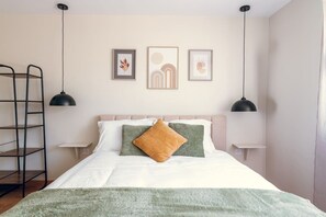 Une chambre à coucher avec un lit, des oreillers, une couverture, une échelle et des œuvres d’art murales.