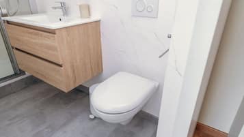 A modern bathroom with a white toilet, a wooden vanity, and a white sink.
