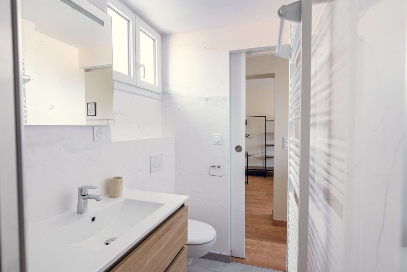 A modern bathroom with a white vanity, a toilet, and a shower area visible through an open door.