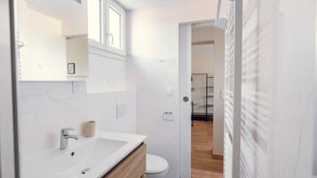 A modern bathroom with a white vanity, a toilet, and a shower area visible through an open door.