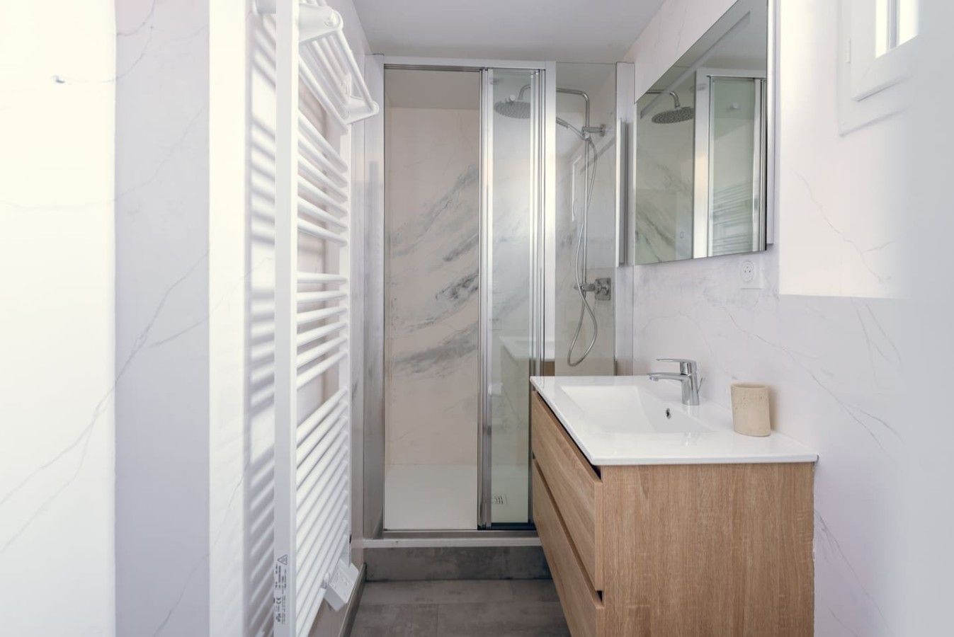 Een moderne badkamer met een douchecabine van glas, een houten wastafelmeubel en een wand betegeld met marmer.